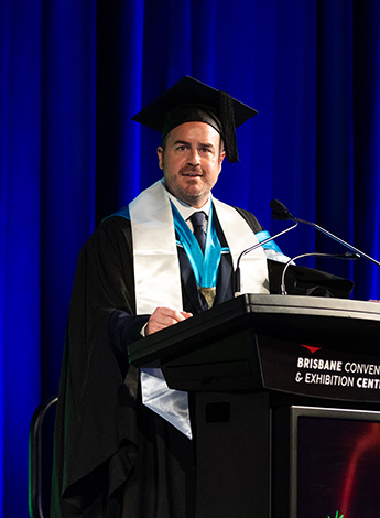 A man in academic regalia is standing behind a podium. 